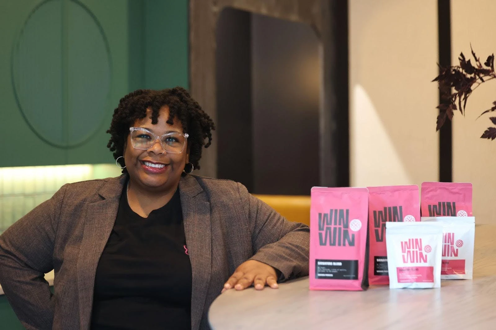 Nikisha Bailey smiling beside pink and white bags of Win Win Coffee on a café counter.
