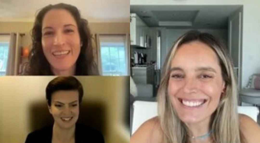 Video call screenshot of a woman with red hair and glasses laughing, next to a smaller inset of a second woman in dark clothing.